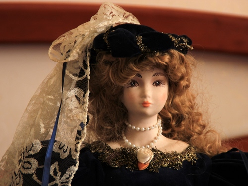 Immagine con bambola, capelli, collana, cappello, velo, pizzo, occhi, nero, perle, ricci, bocca, giocattolo, vestito, nastro, costume, merletti, blu, naso
