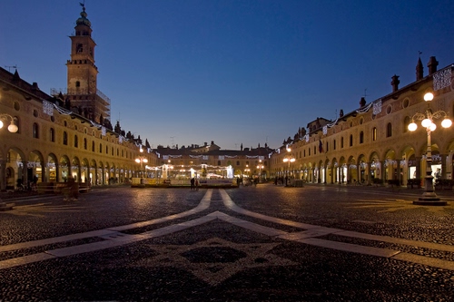 Immagine con piazza, luci, lampioni, cielo, campanile, palazzi, torre, notturno, notte, portici, blu
