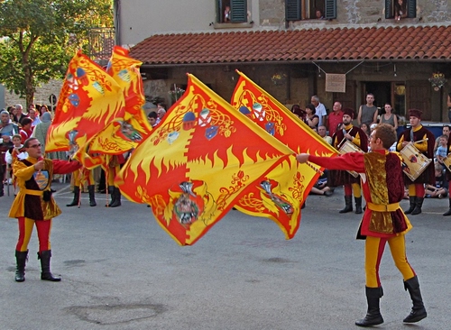 Immagine con rosso, bandiere, giallo, sbandieratori, costumi, albero, persone, tetto, spettatori, piazza, esibizione, manifestazione, tamburi, finestre, tettoia