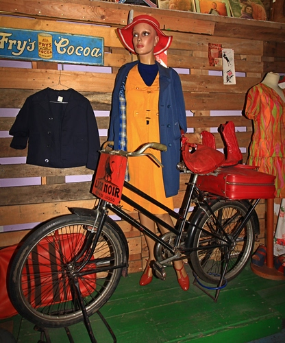 Immagine con bicicletta, manichino, cappello, rosso, valigia, ruote, giallo, nero, vestiti, giacca, legno, bici, negozio, verde, vetrina, insegna, scarpe, abbigliamento